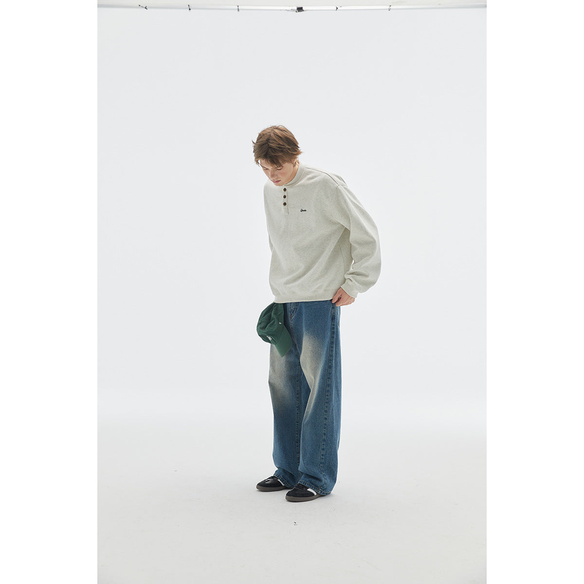 Model wearing an off-white three-button henley sweatshirt with loose blue jeans.