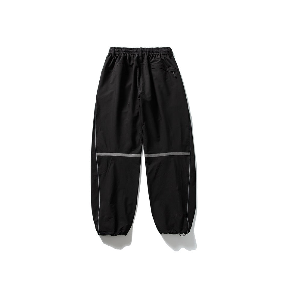 Black loose-fit pants shown from the back, with an elastic waist, zip pocket, reflective knee bands and gathered cuffs.