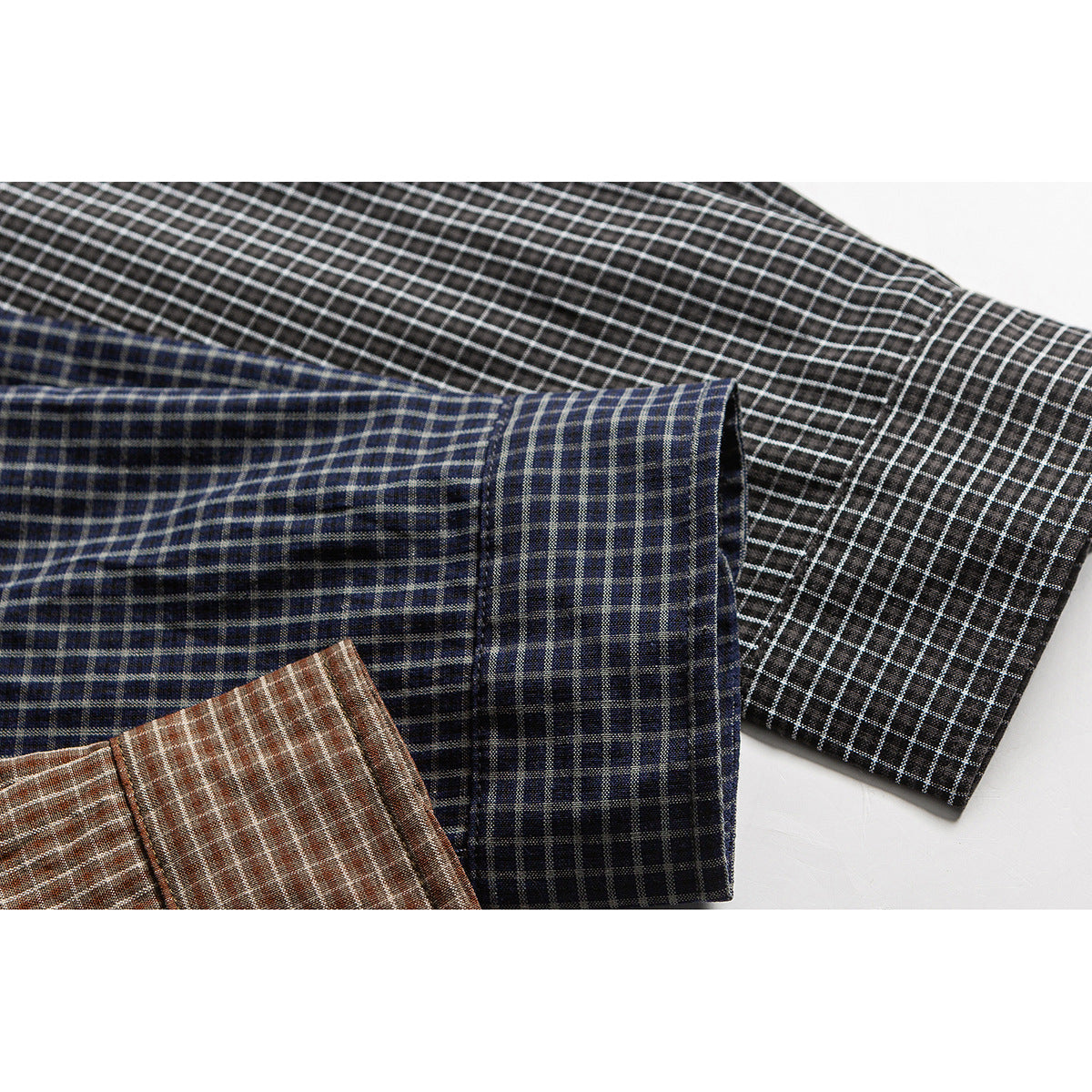 Close-up of overlapping checked shirt sleeves in black, navy, and brown colorways.