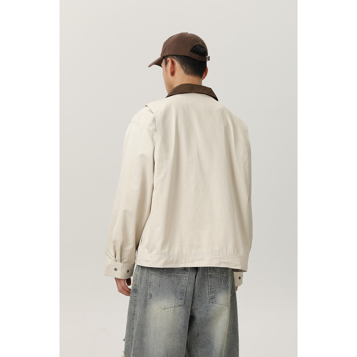 Back view of a model wearing a cream jacket with a brown collar and loose gray jeans.