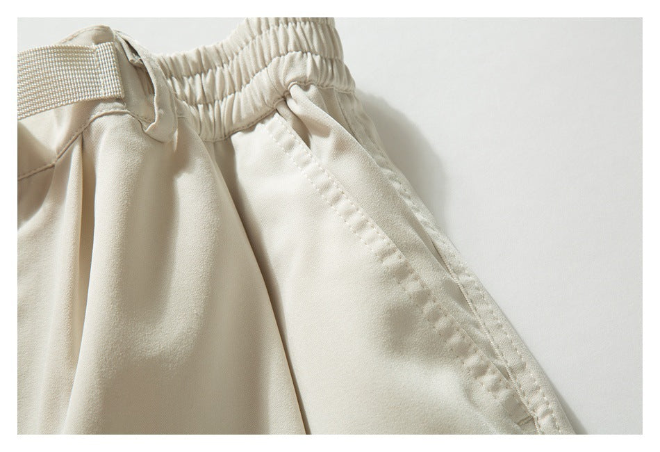 Close-up of light beige trousers showing the gathered elastic waistband, belt loop and stitched seams.