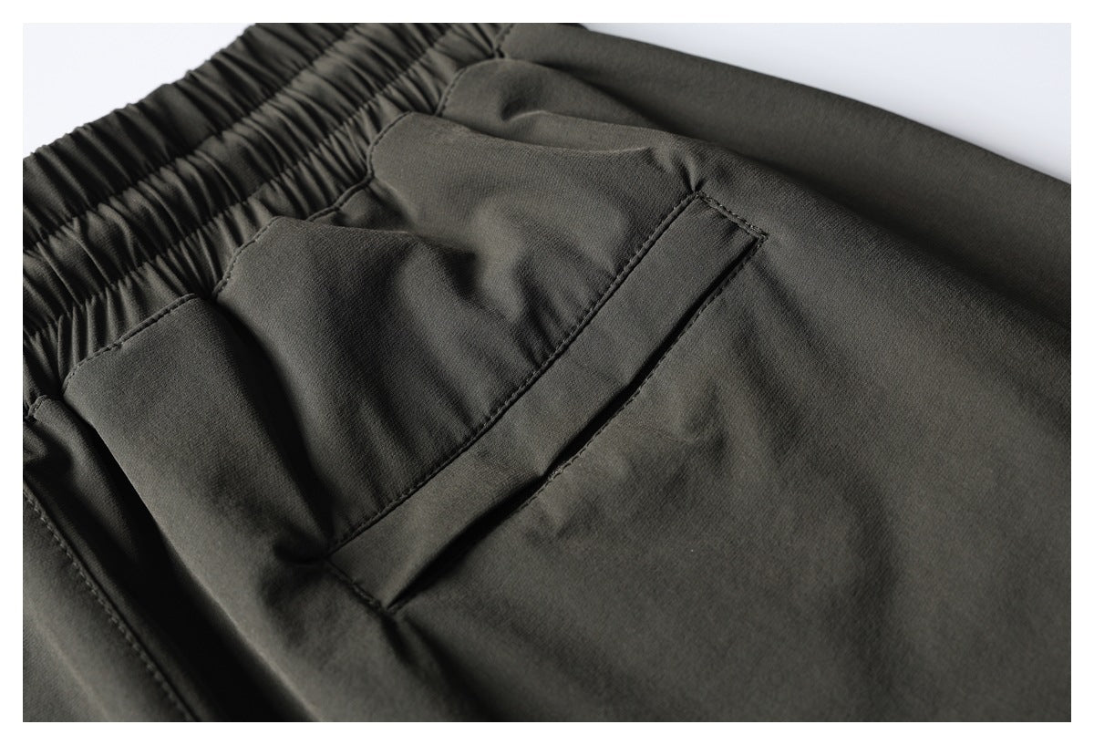 Close-up of dark charcoal pants showing the elastic waistband and a slanted front pocket.