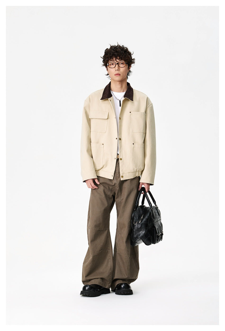 Full-length model facing forward in a cream jacket with dark collar and wide brown trousers.