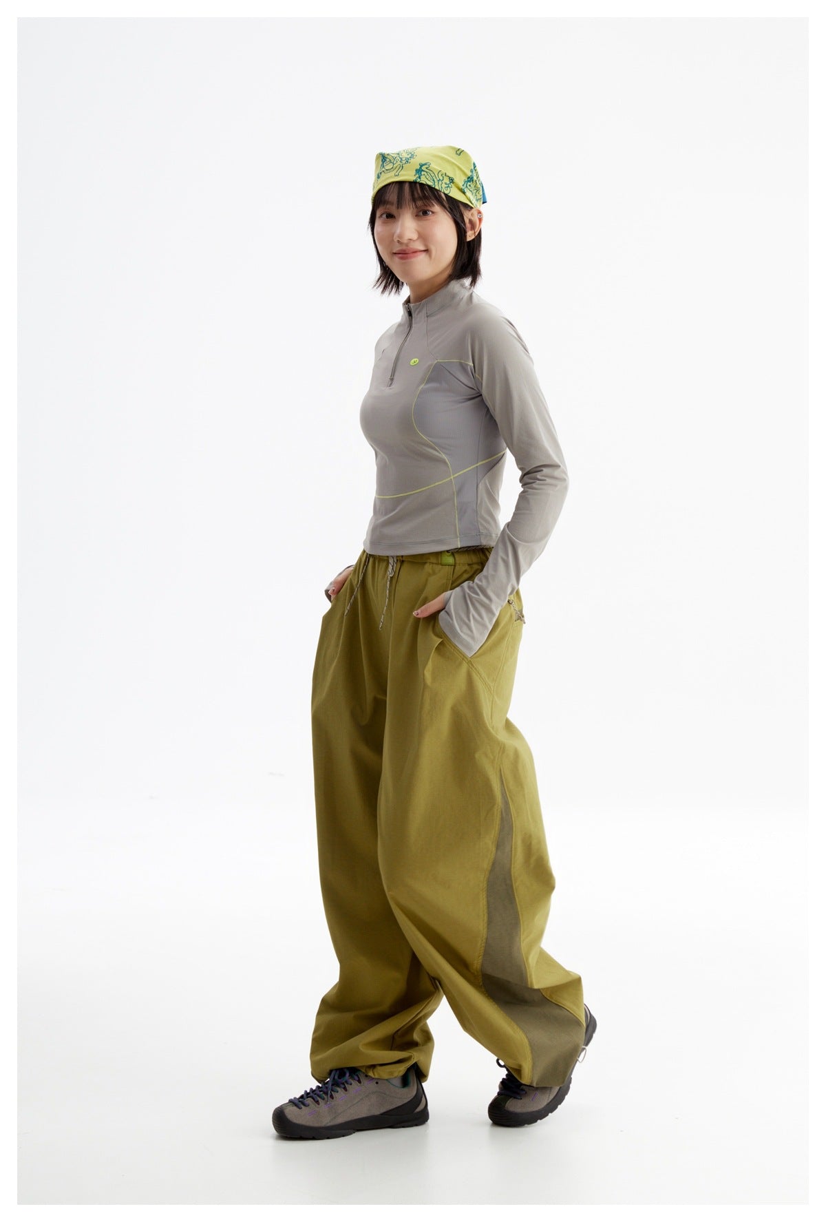 Model in a side pose wearing a gray quarter-zip top with lime piping and olive wide-leg pants.