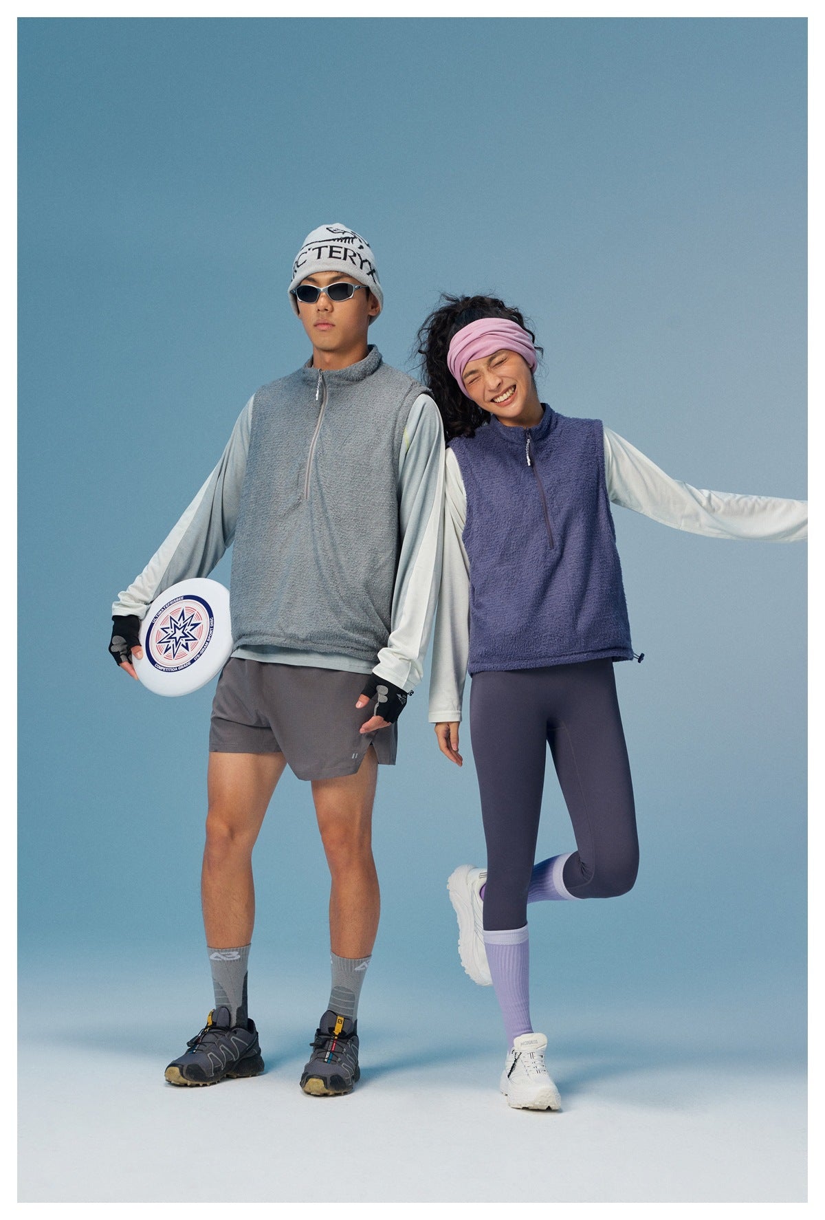 Two models wear gray and purple sleeveless zip vests over pale long-sleeve tops.