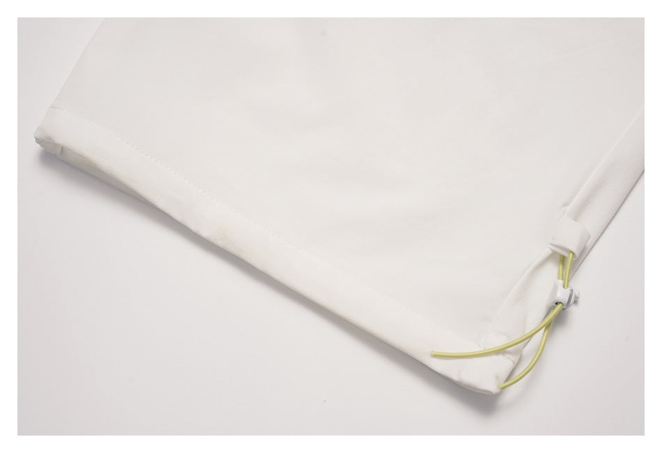 Close-up of a white garment hem with pale yellow cords and a small white toggle.