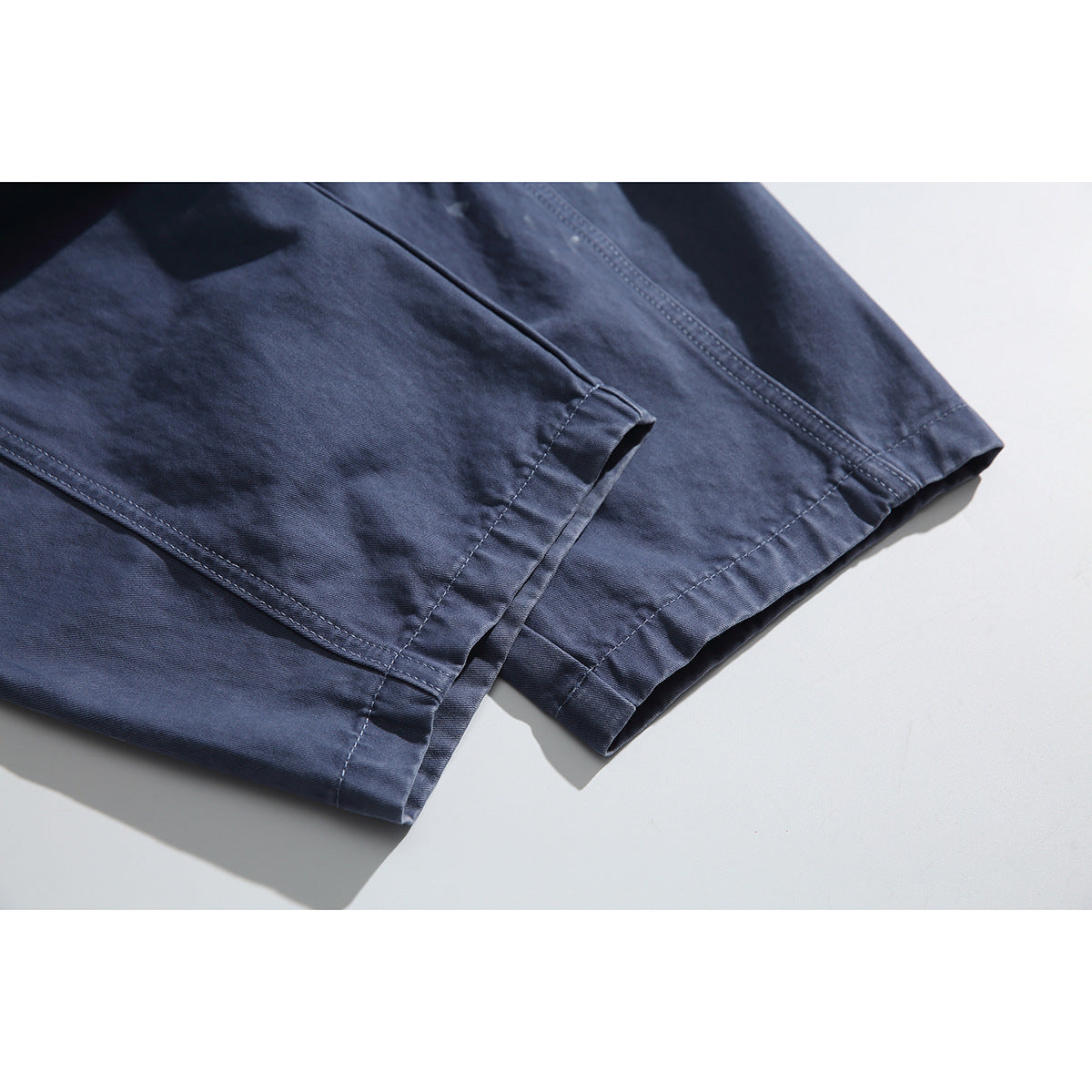 Close-up of the stitched hems on blue-gray pants laid flat.