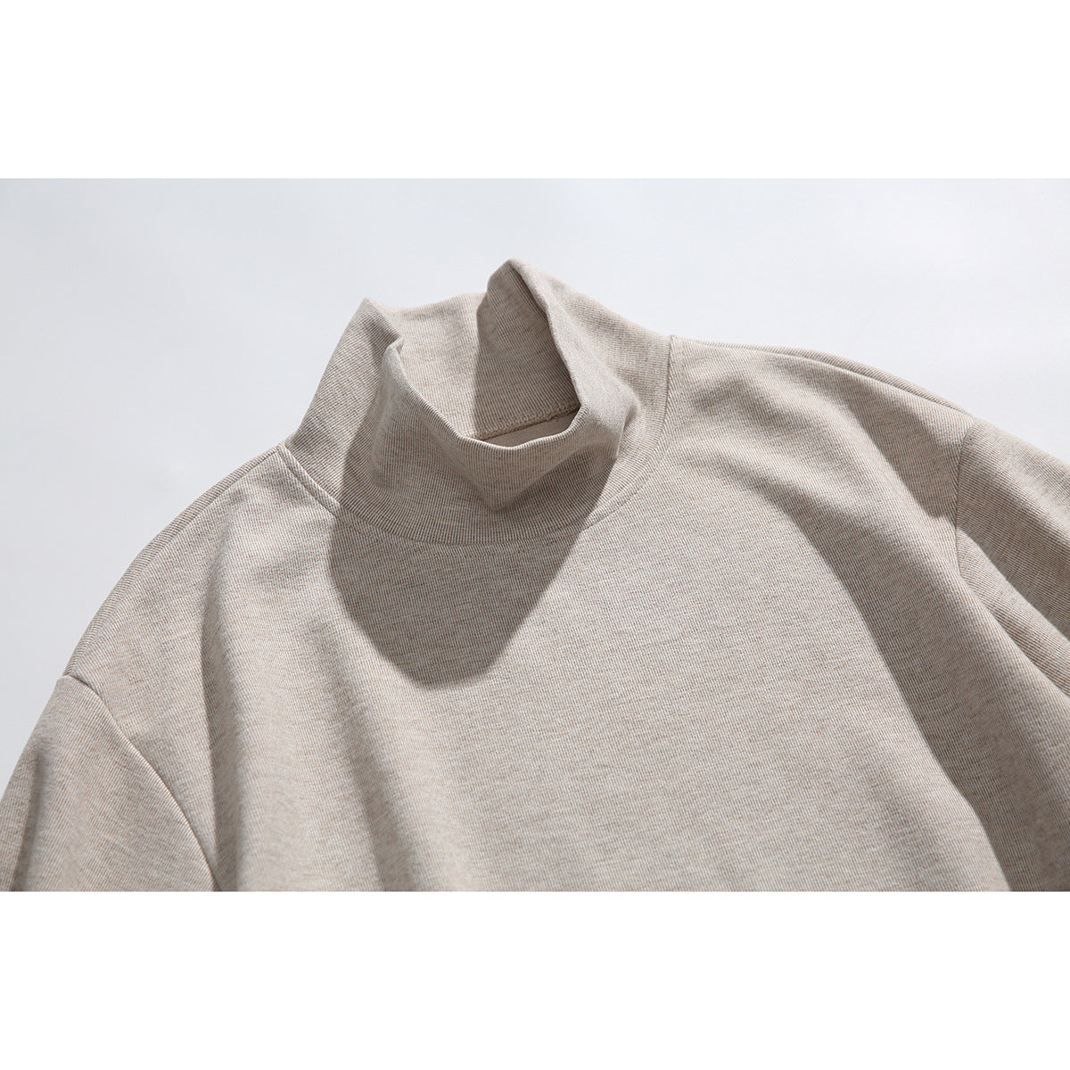 Close-up of a light beige heather top showing its high mock neck and upper front.