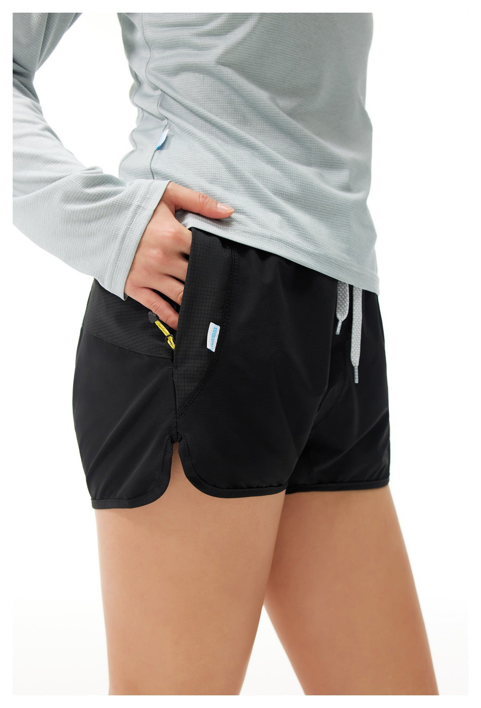 Close view of black running shorts worn by a model, showing the side pocket, yellow zipper pull, and drawstring.
