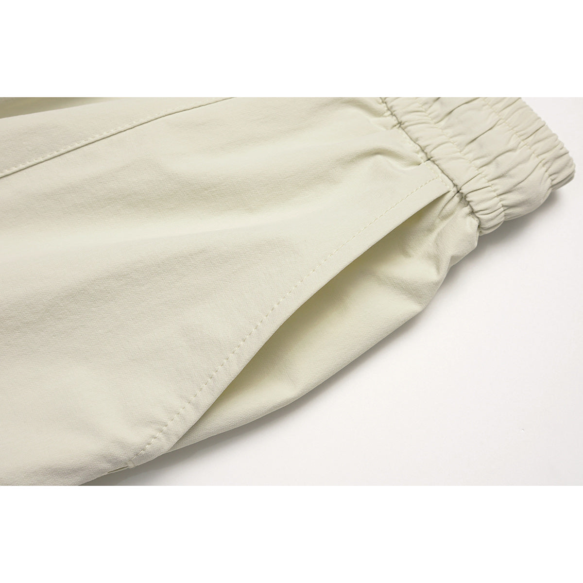 Close-up of off-white pants showing a stitched pocket opening and elastic waistband.