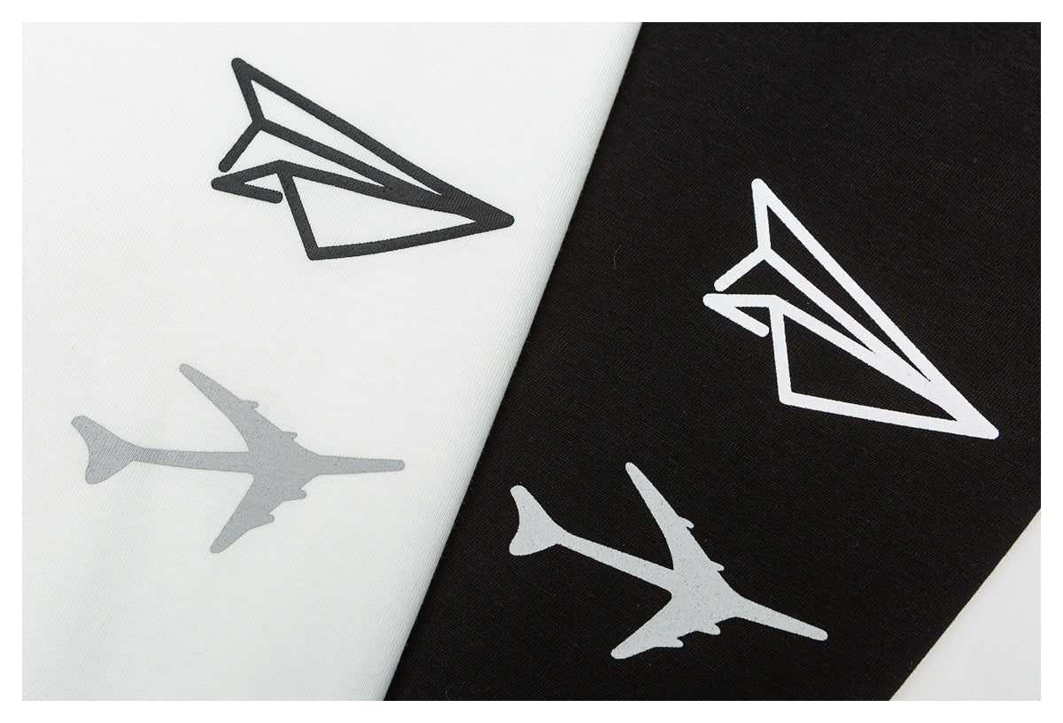 Close-up of white and black garment colorways, each printed with a stylized paper airplane graphic.