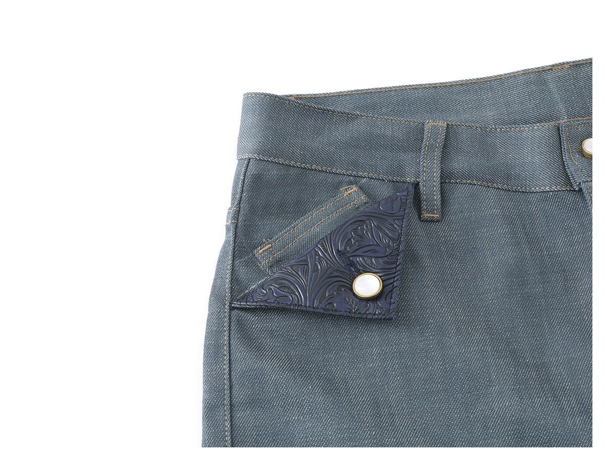 Close-up of blue-gray trousers showing the front waistband, button, belt loop, and embossed floral pocket trim.