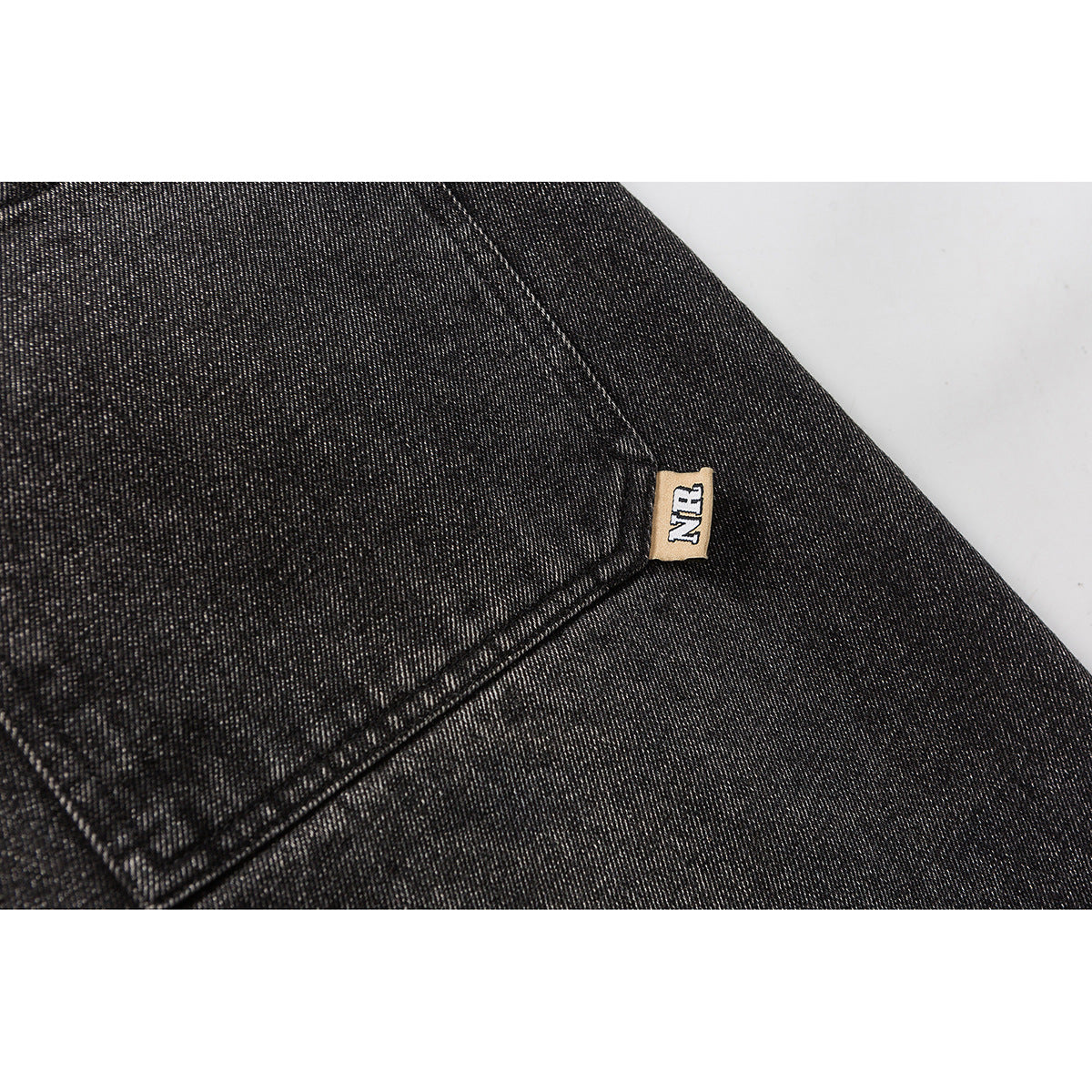 Close-up of a stitched pocket seam and small fabric tag on dark washed jeans.