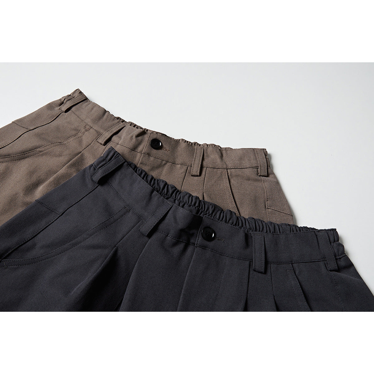 Close-up of charcoal and taupe shorts waistbands with buttons, belt loops and front pleats.