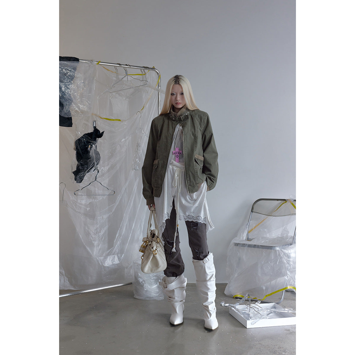 Full-length model wearing an olive jacket with a white layered top, dark trousers and tall white boots.