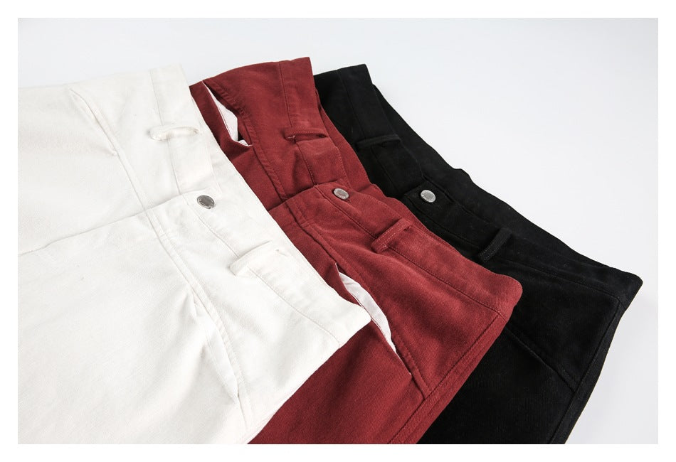 Three pairs of trousers in ivory, burgundy, and black, folded to show the waistbands, buttons, and pocket details.