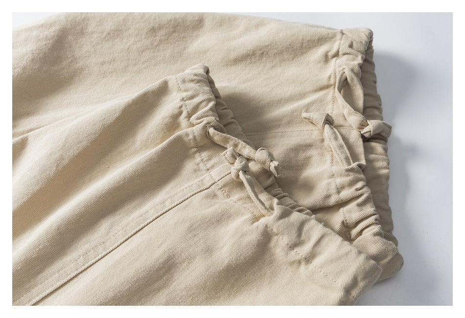 Close-up of beige trousers with a gathered waistband and tied fabric drawstring.