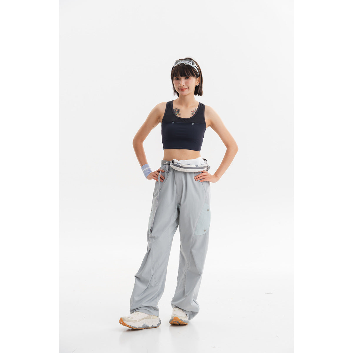 Model wearing a black cropped sports top and loose gray pants against a white background.