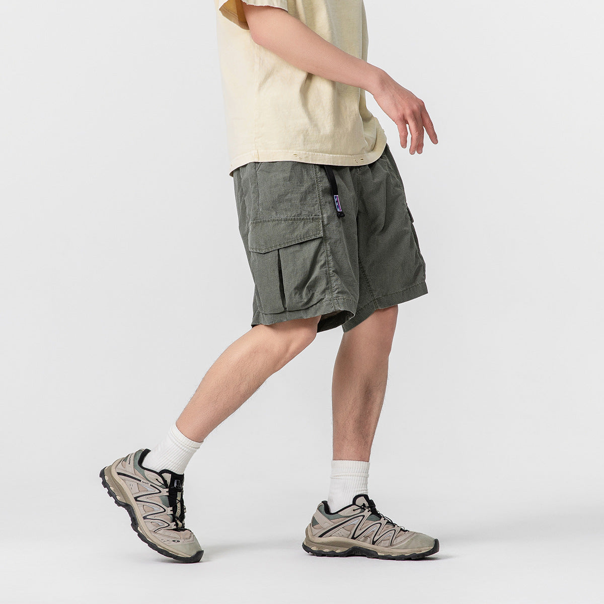 Side view of a model wearing loose charcoal-gray cargo shorts with a large flap pocket.