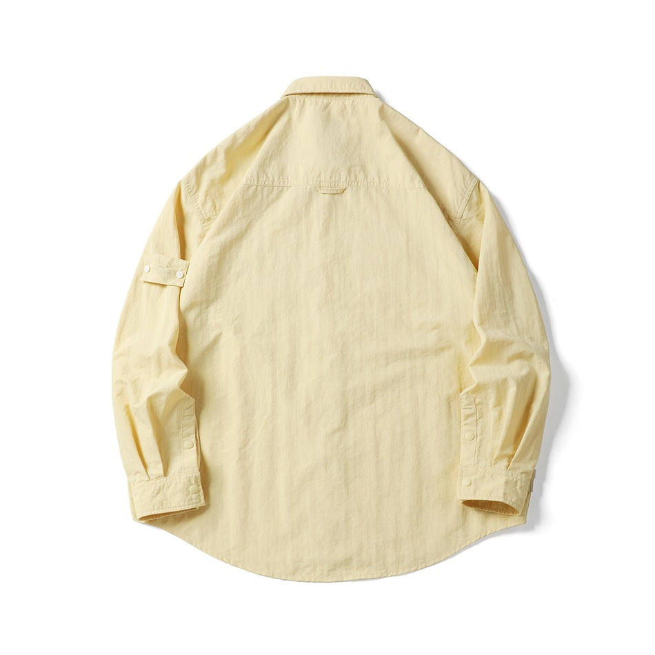 Back view of a pale yellow long-sleeve shirt laid flat, showing a curved hem and buttoned cuffs.