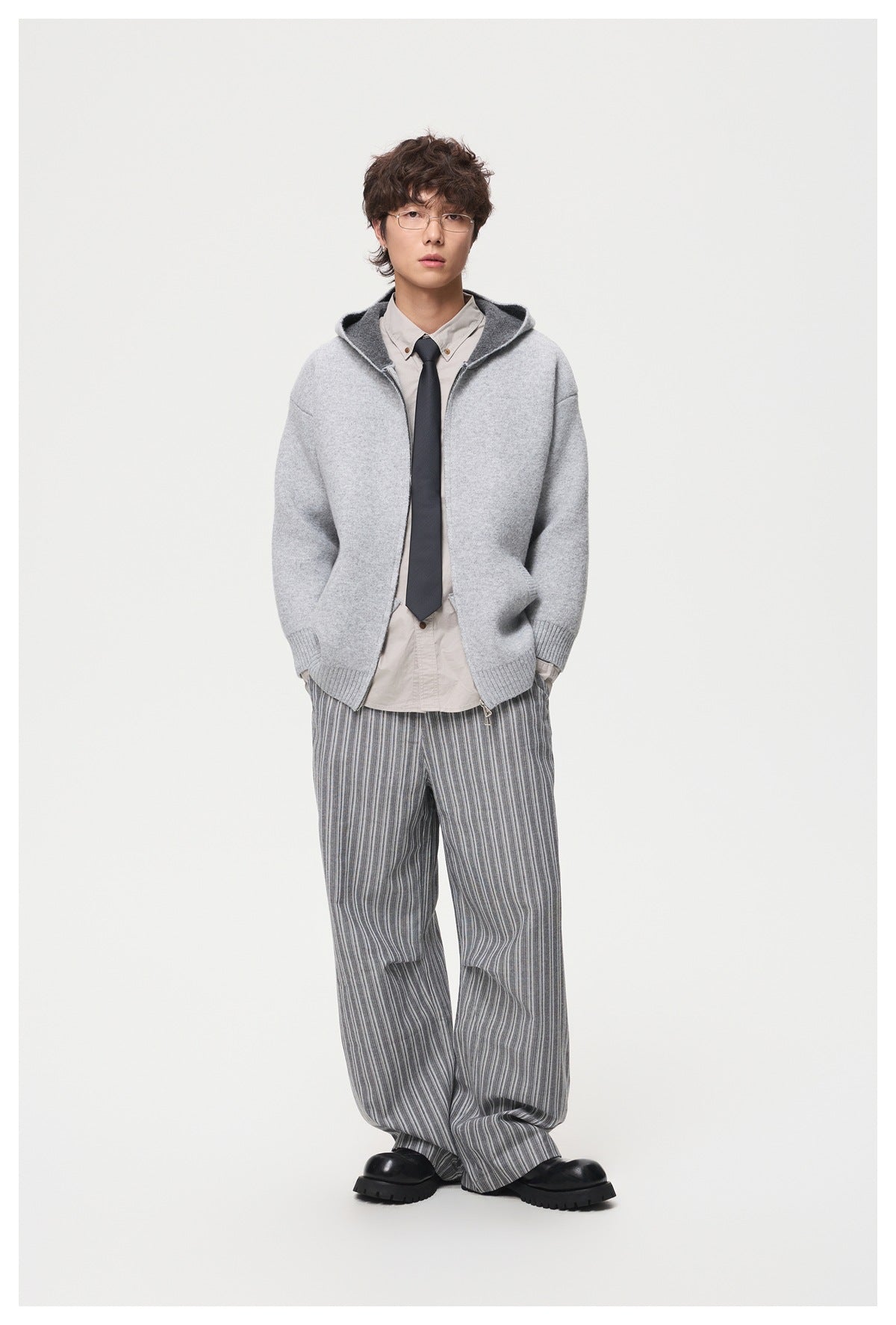 Full-length view of a model wearing a light gray hooded zip cardigan with striped wide-leg trousers.