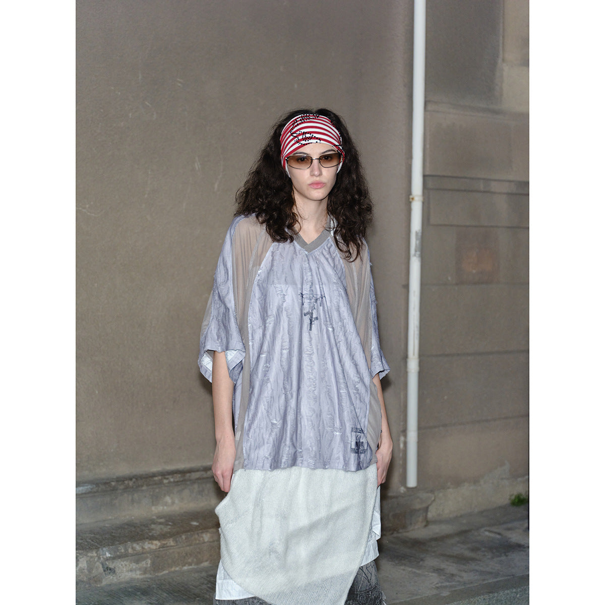 Front view of a model in a loose pale gray V-neck top with sheer taupe sleeves and a layered white skirt.