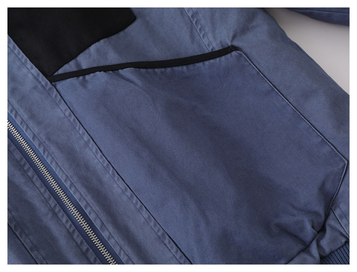 Close-up of a blue-gray jacket pocket with black trim beside the front zipper.