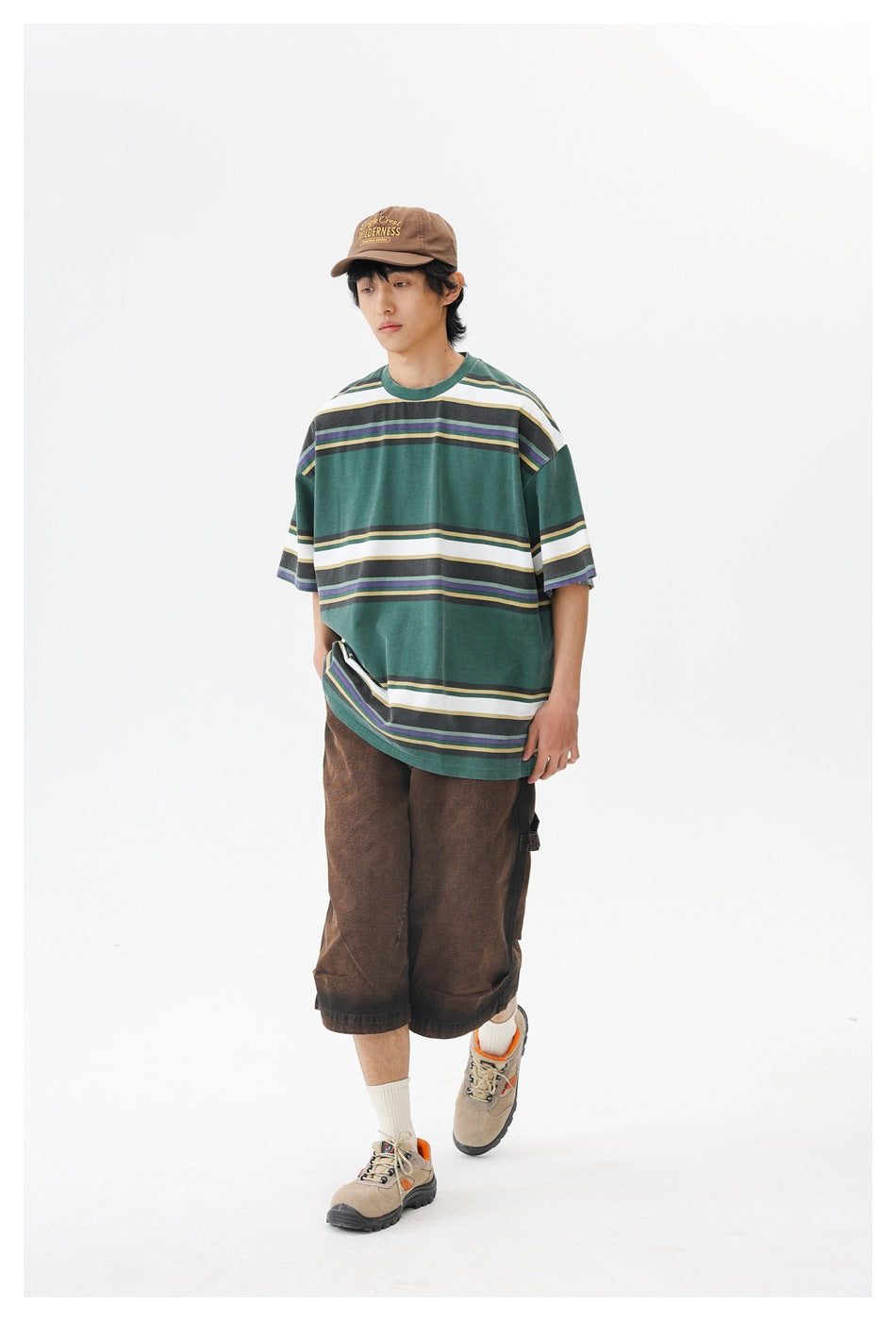 Model in a forest-green oversized T-shirt with broad white and narrow charcoal, purple, and tan stripes, shown from the