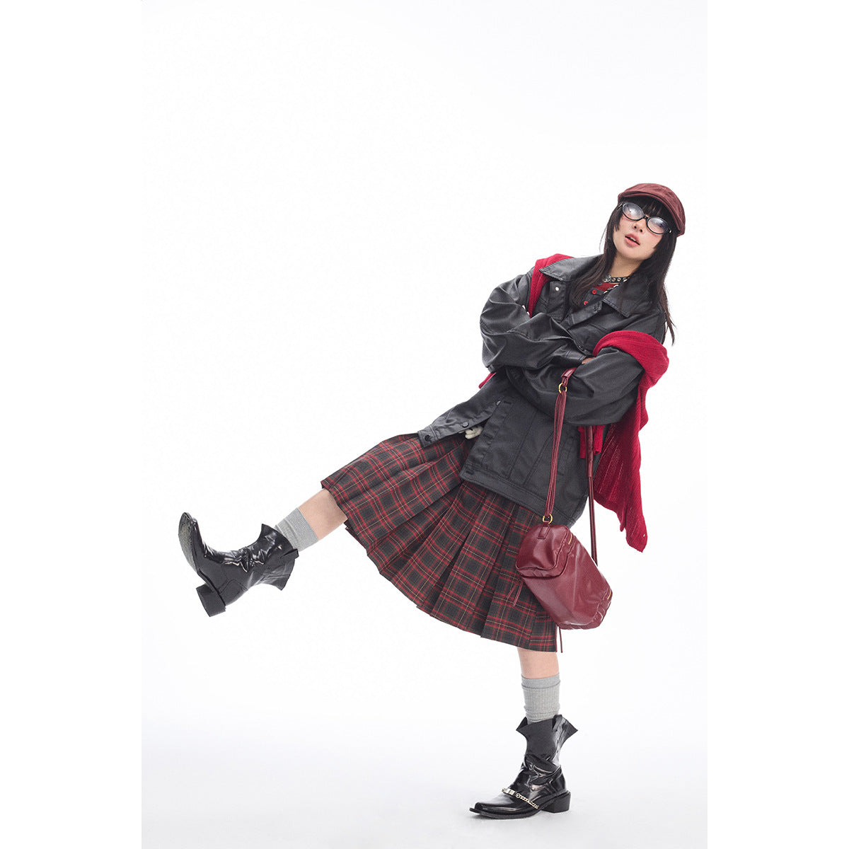 Model in a charcoal jacket, red-and-black plaid pleated skirt, red knit layer, burgundy cap, and black boots.