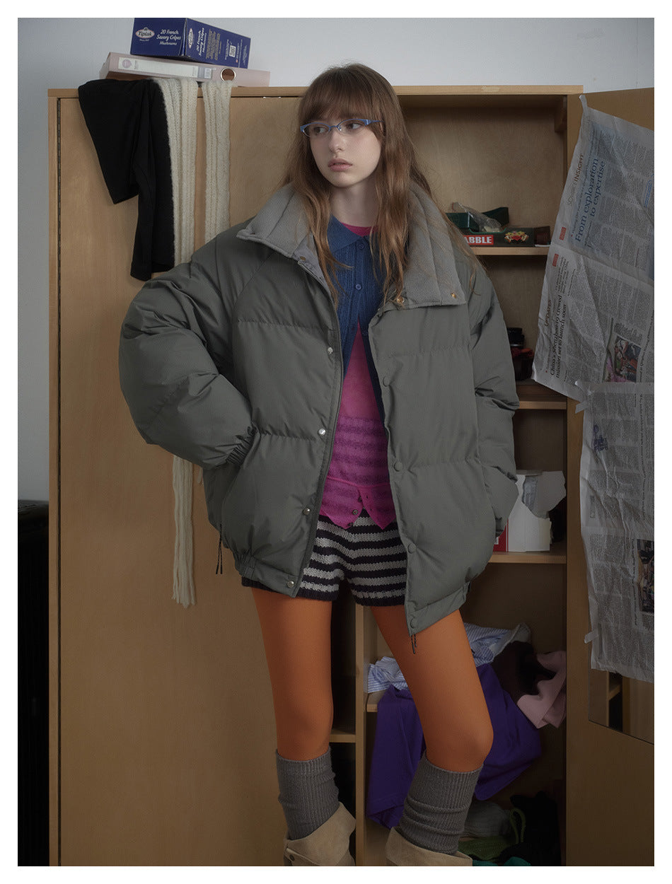 Model wearing an oversized charcoal-gray puffer jacket with snap closures, styled over colorful layers; front view.