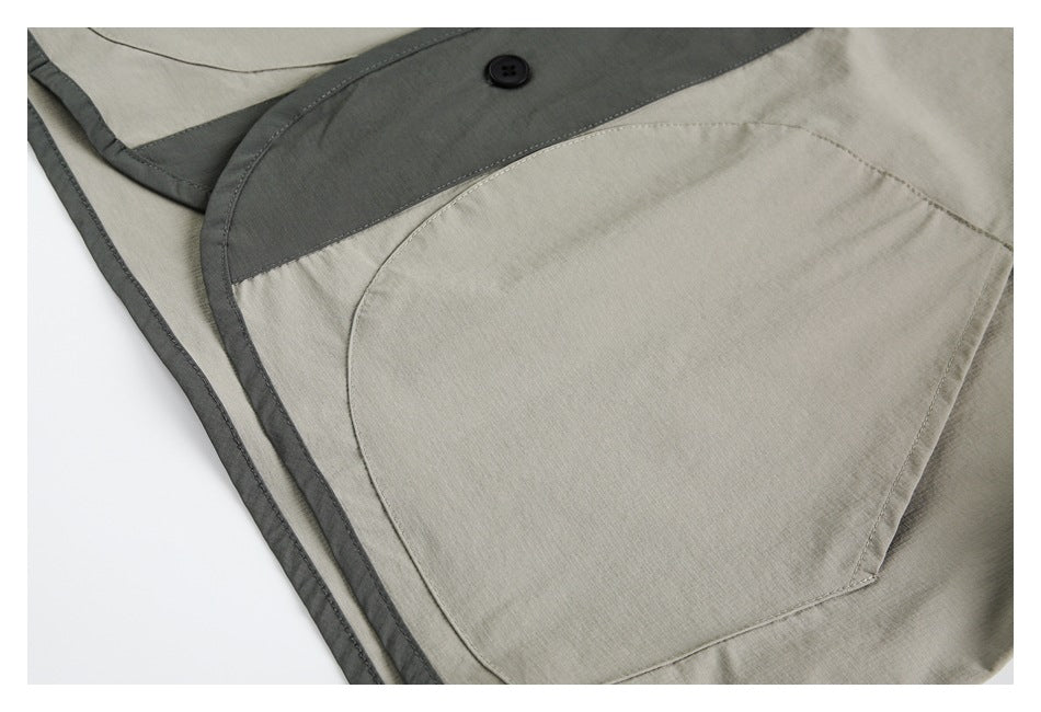 Close-up of a large curved patch pocket on light gray fabric beside dark contrast trim and a button.
