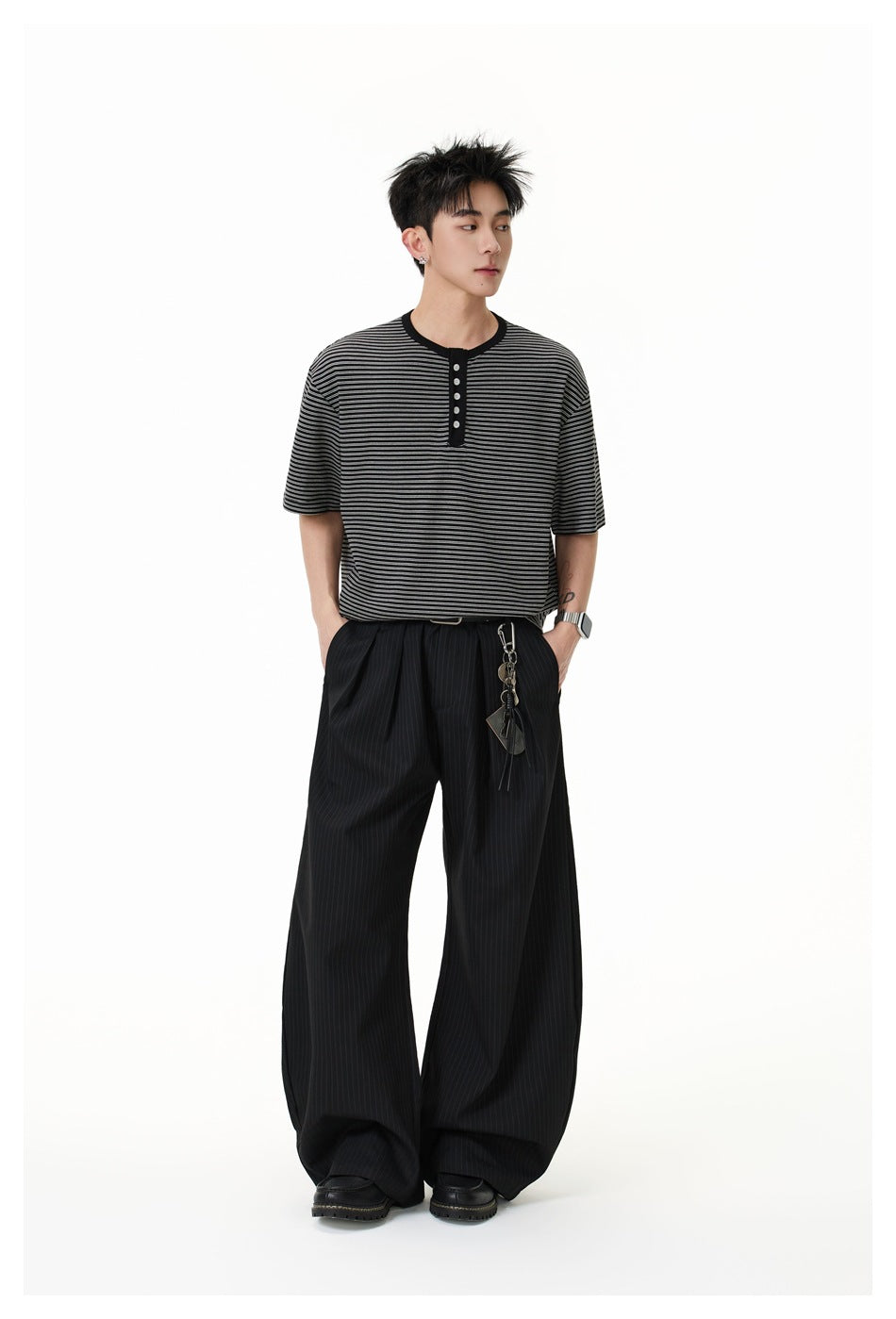 Full-length view of a model wearing a black and gray striped henley with loose black pinstripe trousers.