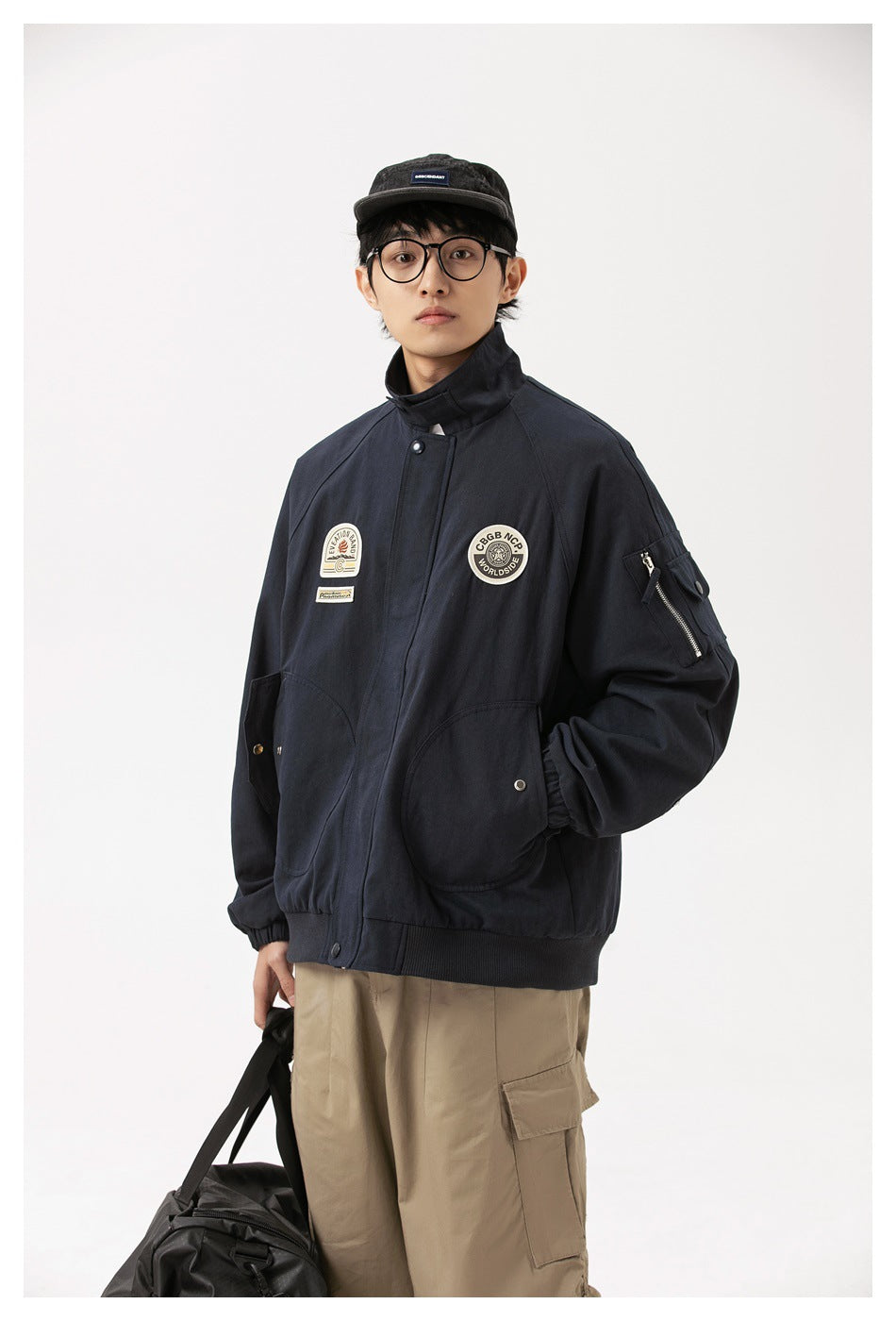 A model wears a dark navy high-collar jacket with chest patches, large pockets and a zippered sleeve pocket.