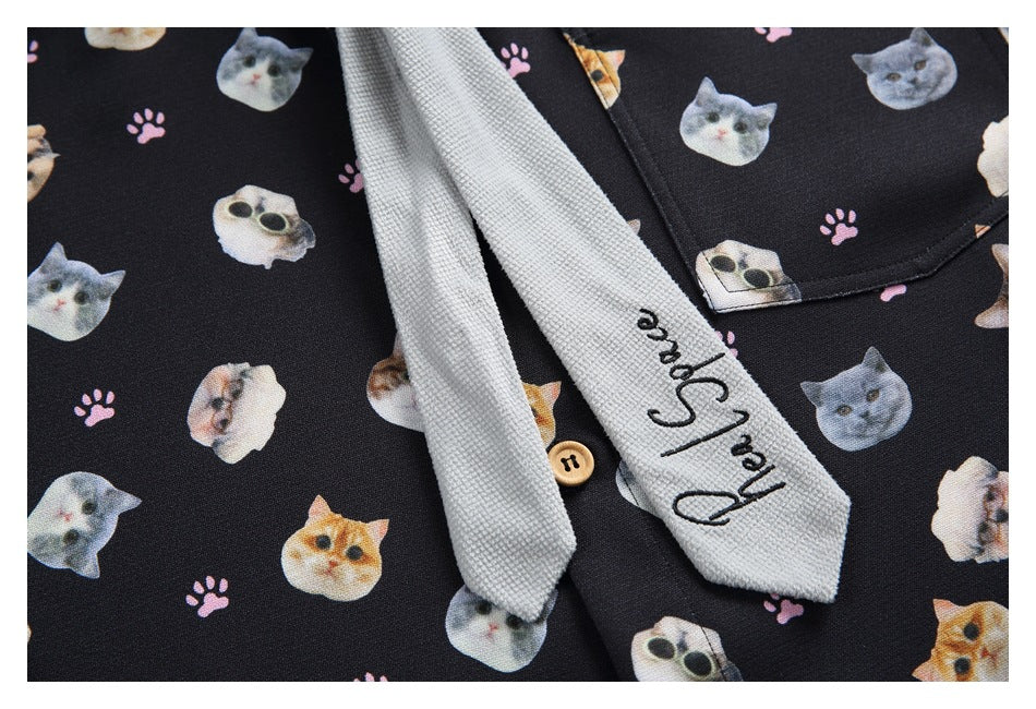 Close-up of the black cat-and-paw-print shirt, gray tie, and chest pocket with a wooden button.
