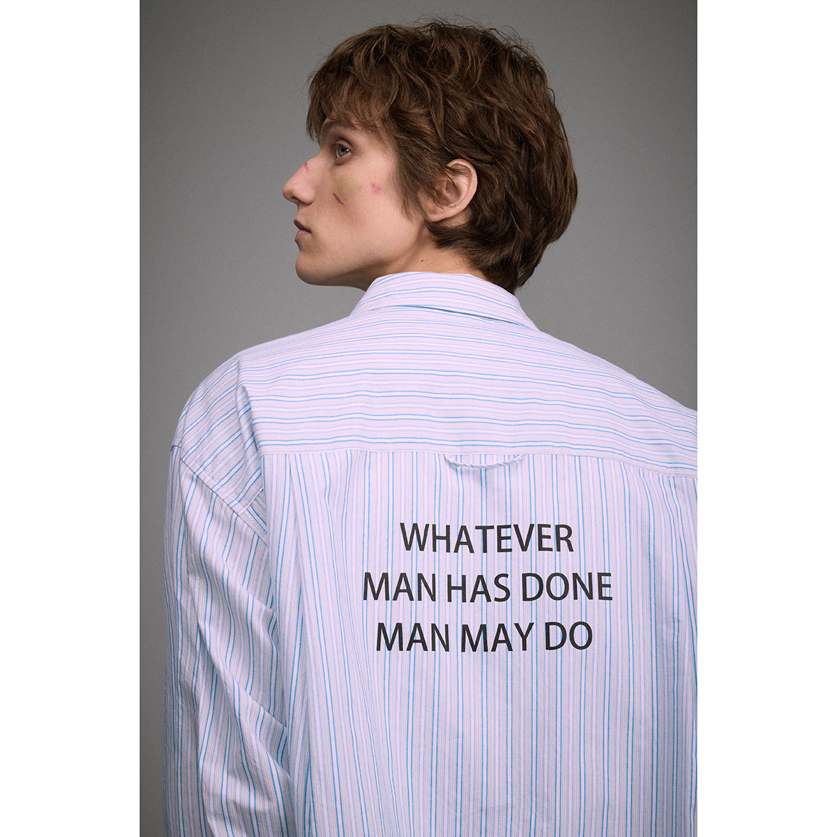 Back view of a blue-and-white striped shirt with the printed slogan “WHATEVER MAN HAS DONE MAN MAY DO.”