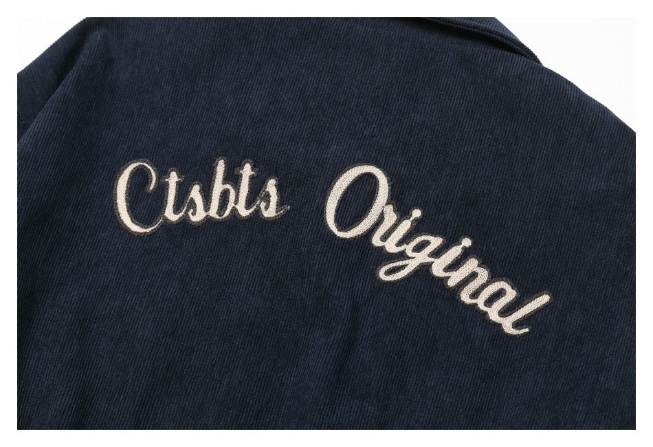 Close-up of large white script embroidery reading “Clubs Original” on dark navy fabric.
