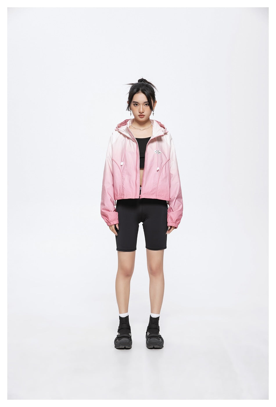 Model wearing a pink gradient cropped hooded zip jacket with black top and black bike shorts, front view