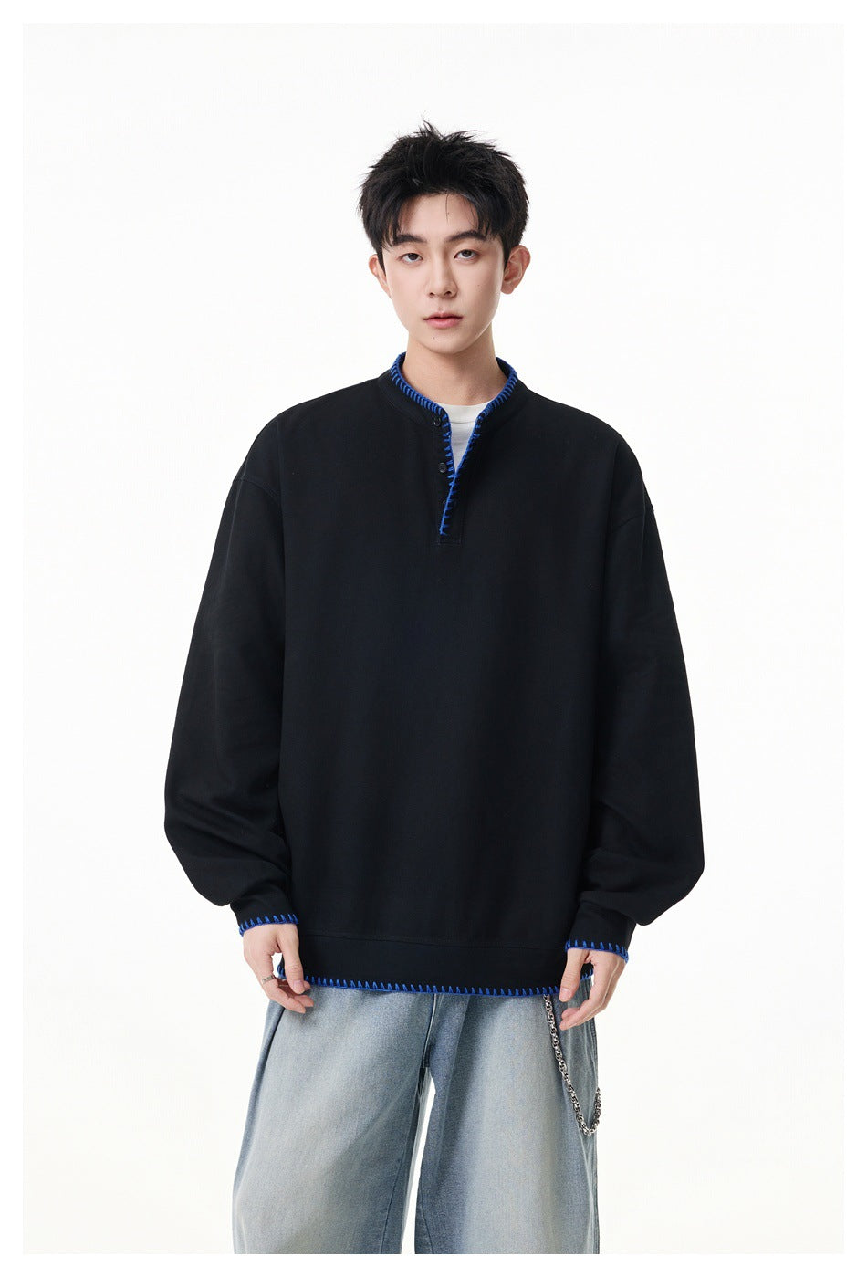 Front view of a model wearing a black oversized pullover with a short button placket and bright blue stitched trim.