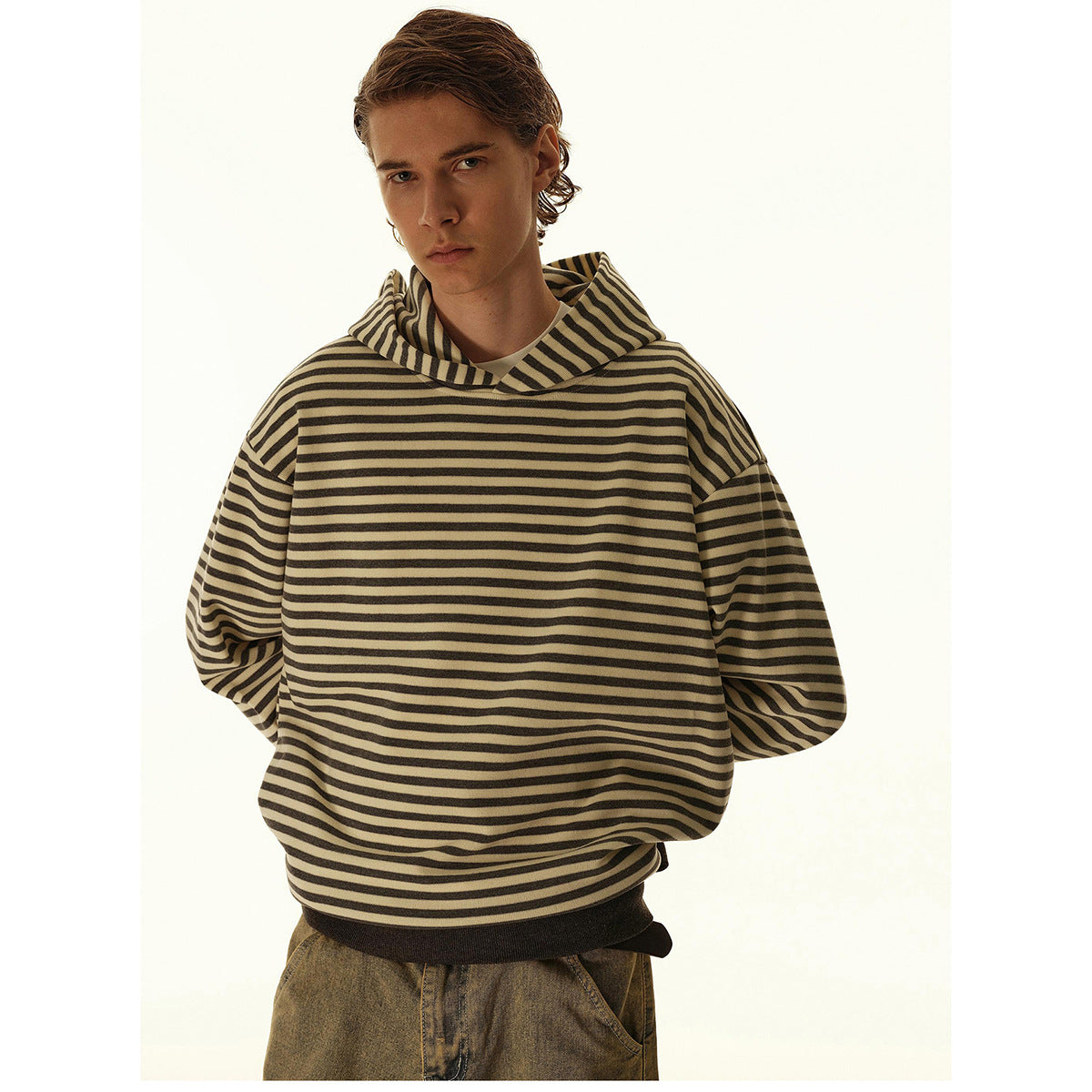Front view of a model wearing a loose beige and dark striped hooded sweatshirt with a dark ribbed hem.