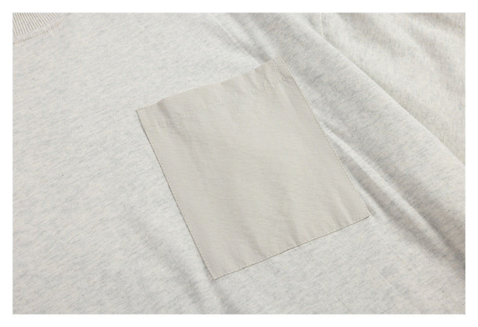 Close-up of a square light beige patch pocket sewn onto a pale heather-gray garment.
