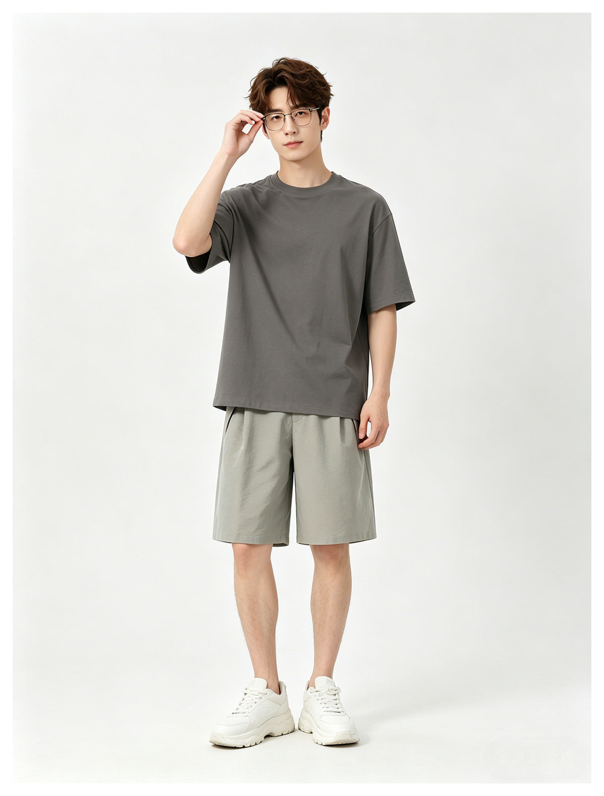 Man in a gray T-shirt, khaki pleated knee-length shorts and white sneakers, standing front view