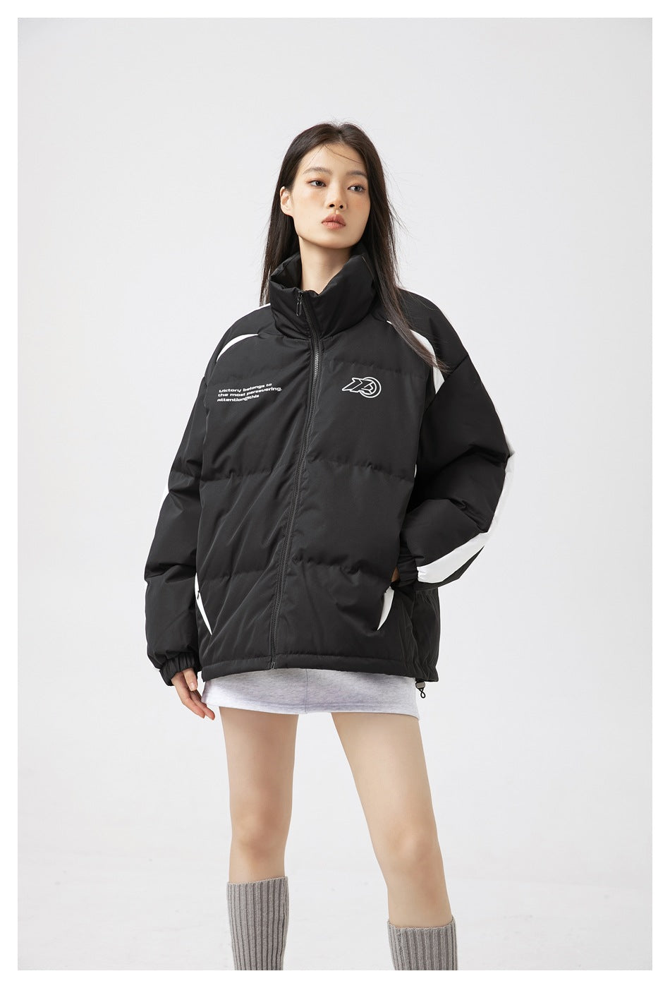 Model wearing a black padded zip jacket with a high collar, white sleeve stripes, and small white chest graphics.