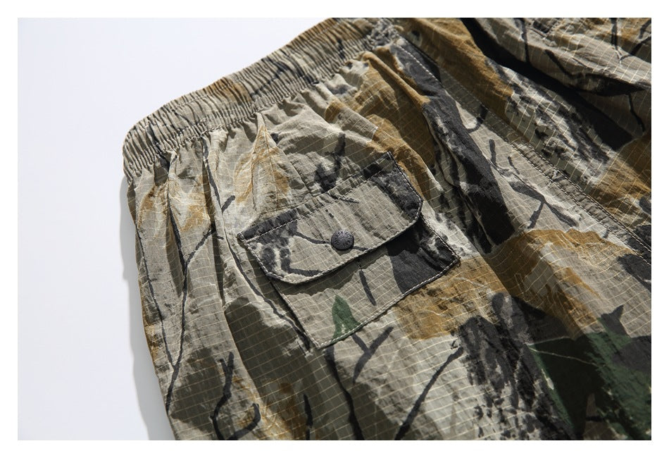 Close-up of camouflage shorts showing an elastic waistband and a button-flap cargo pocket.