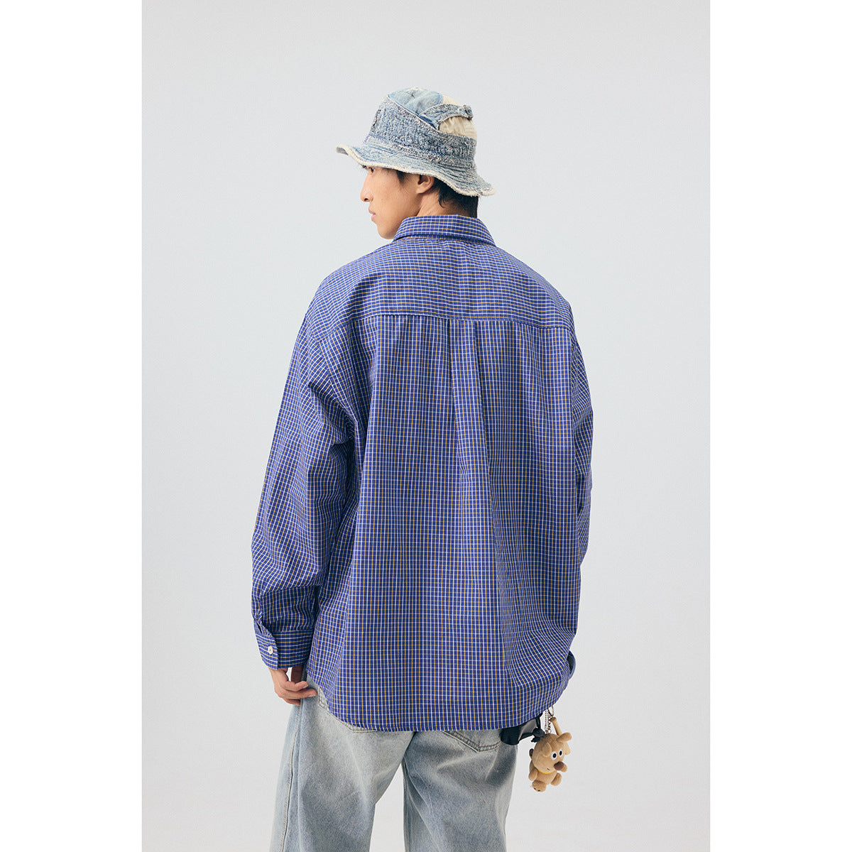 Back view of a model wearing a blue checked shirt with a back yoke and center pleat.