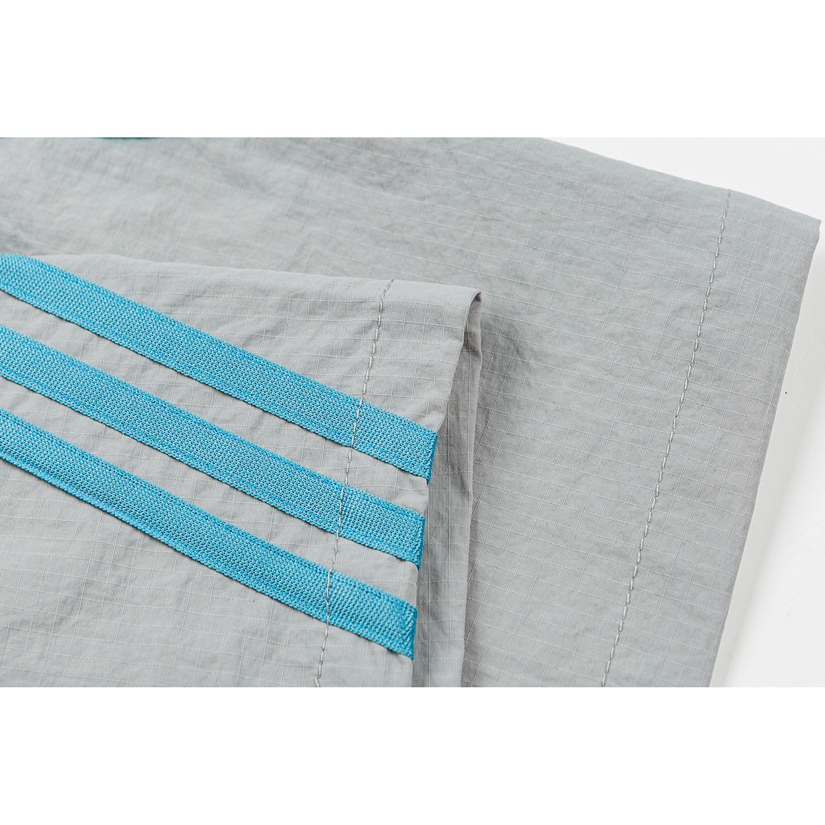 Close-up of gray shorts with three bright blue woven side stripes and stitched seams.