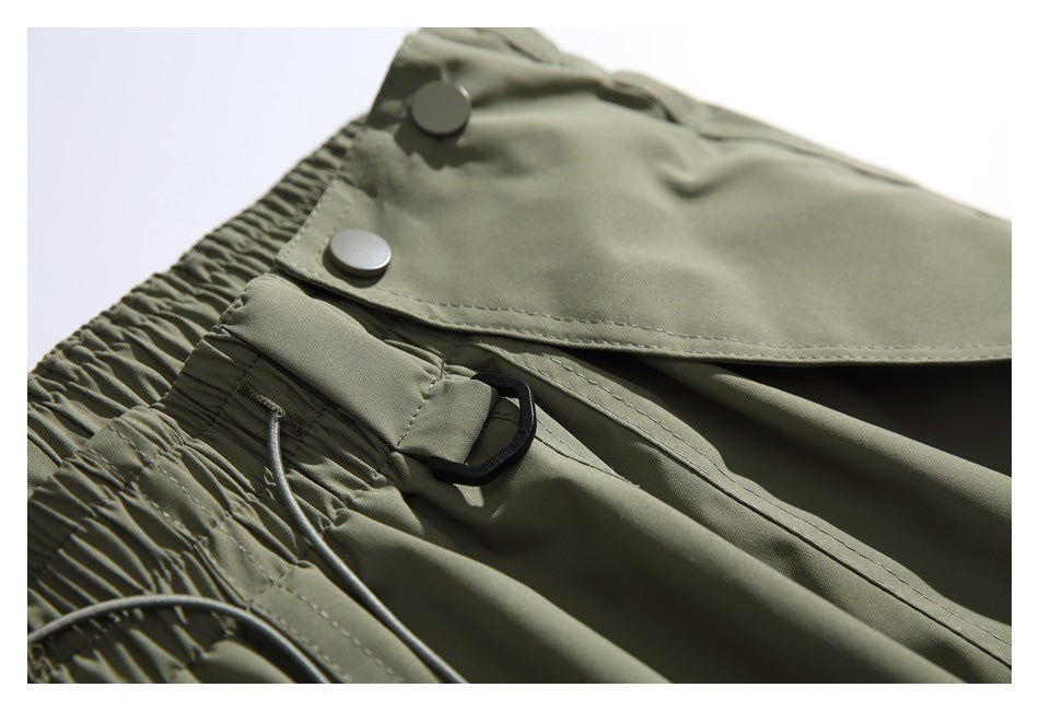 Close-up of the olive-gray pants' snap-button flap, black loop and gathered elastic waistband.