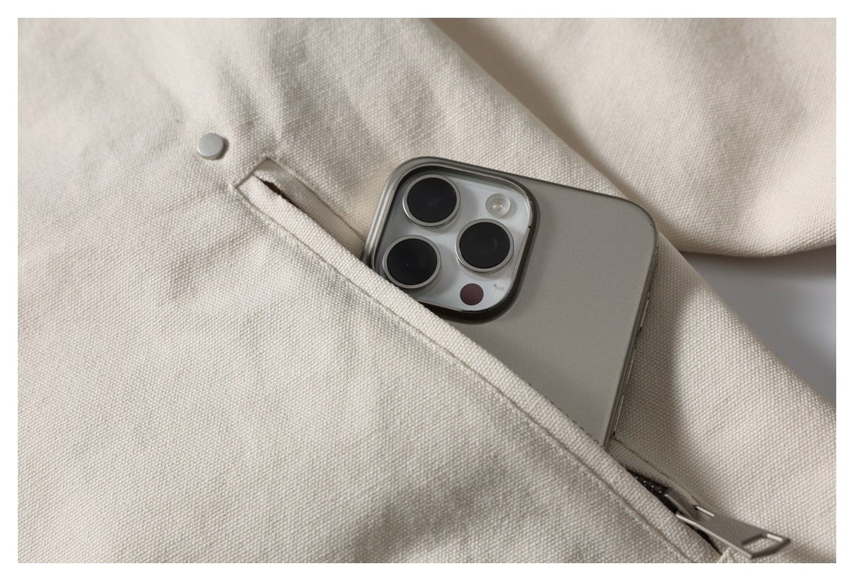 Close-up of an ivory jacket pocket holding a smartphone, with a metal snap and zipper visible.