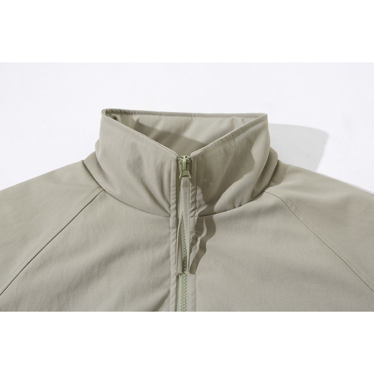 Close-up of a light beige jacket’s tall stand collar and front zipper.