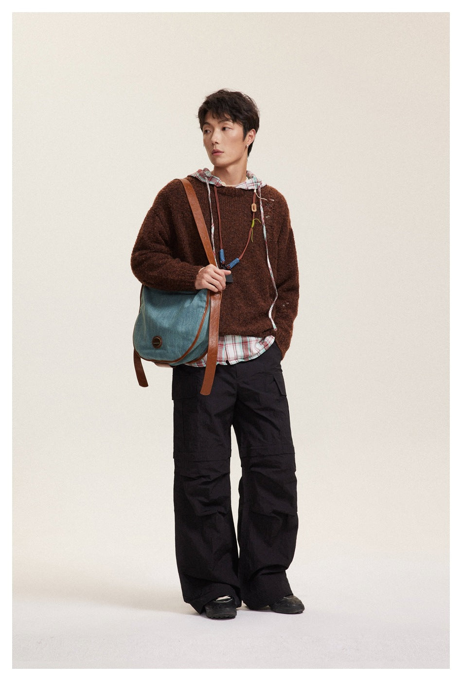 Model wearing the brown distressed knit sweater over a plaid hooded layer with black cargo pants, looking sideways