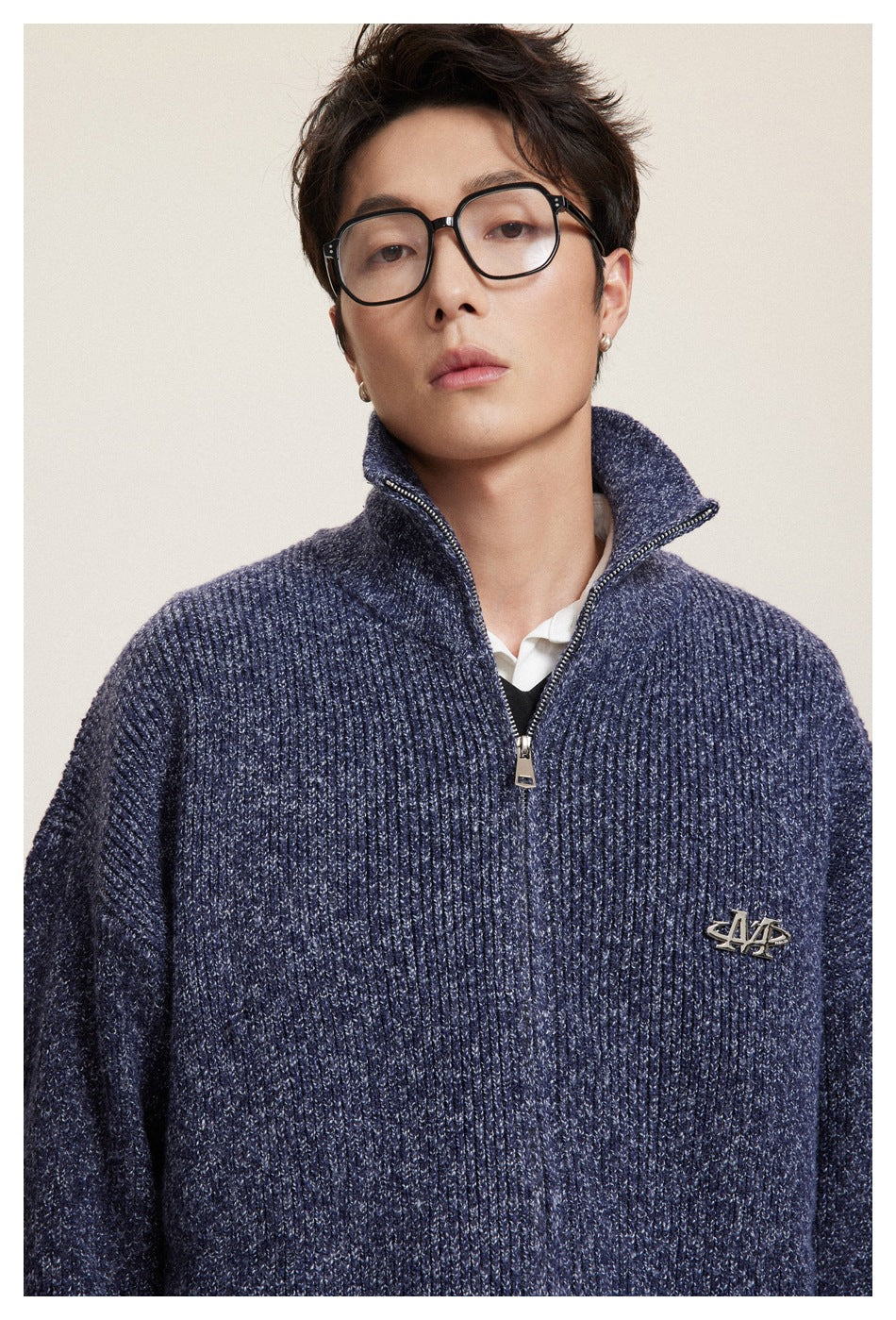 Close-up of a model wearing a navy ribbed zip-neck sweater, showing its raised collar, zipper, and chest emblem.